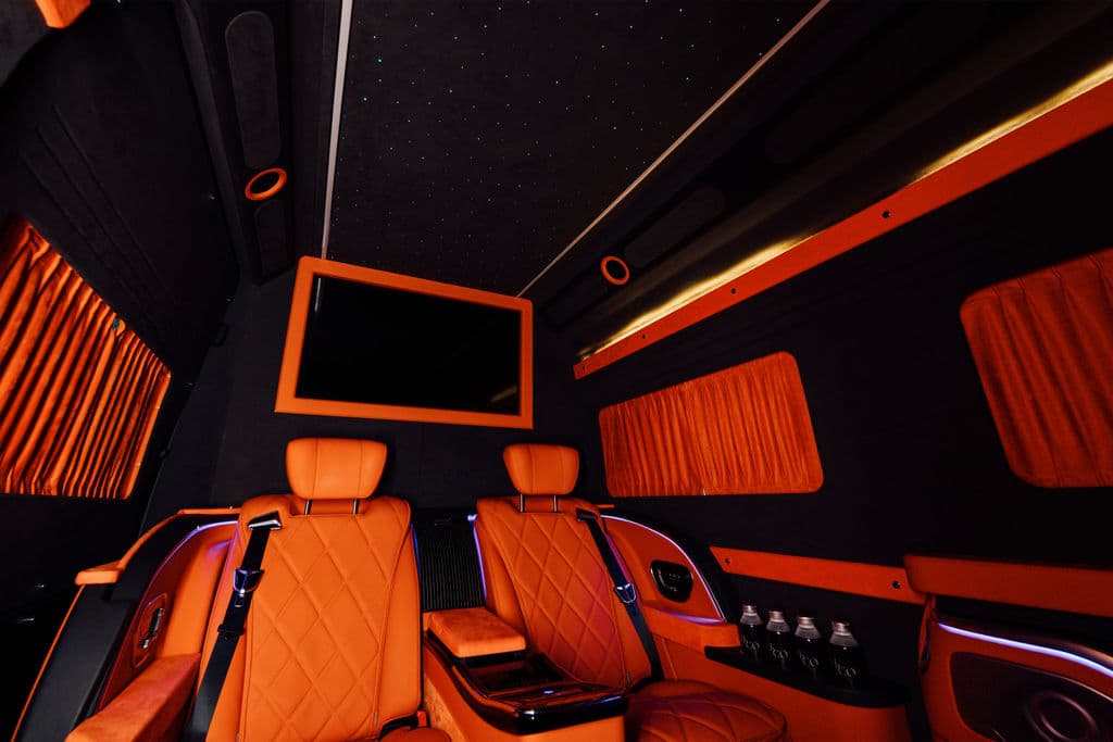 Rear cabin of a Mercedes-Benz Sprinter with orange quilted seats, curtained windows, and a starlight ceiling